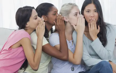 Four friends share secrets, whispering what is gossip. One girl looks surprised as the whispers continue.