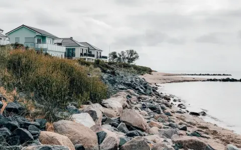 Häuser am Hang über einem steinigen Strand. Ein ruhiger Ort, der zu den Fehmarn Geheimtipps zählt.