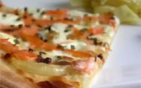 Tranche de flammekueche saumon, oignons et fromage, avec une salade verte en arrière-plan.