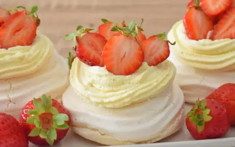 Mini torty pavlova z bitą śmietaną i świeżymi truskawkami.