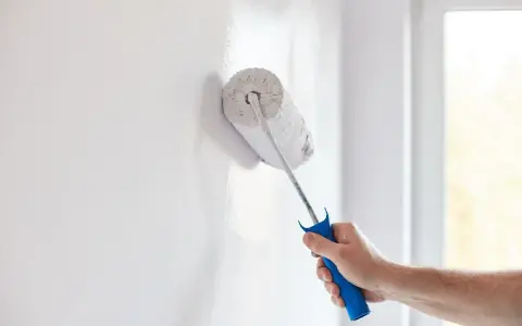 Mano con rodillo pintando una pared blanca, renovando el hogar.