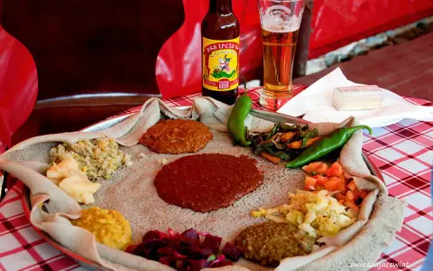 Tradycyjna kuchnia etiopska na płaskim chlebie injera, z różnymi gulaszami, warzywami i papryczkami. Obok piwo.