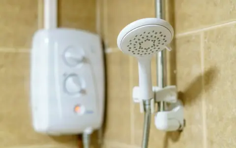 Ein weißer Boiler für die Dusche mit Reglern und eine Duschbrause an der Wand.