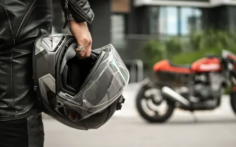 Motociclista con casco, simbolo di sicurezza e certificazione casco moto. Moto rossa sfocata sullo sfondo.