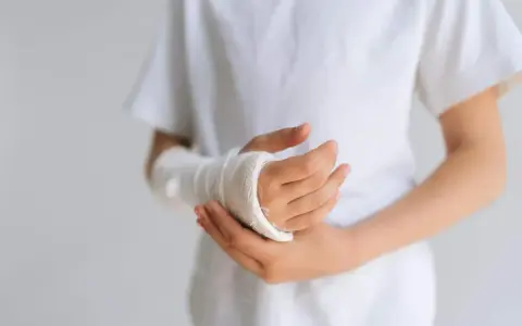 Dziecko z opuchlizną po zdjęciu gipsu nadgarstek, w białej koszulce, z ręką owiniętą bandażem.