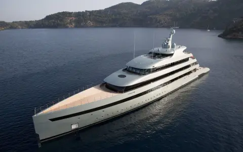 Un yacht de luxe gris clair navigue dans une baie. Le choix couleur coque bateau est élégant, contrastant avec le bleu profond de l'eau.
