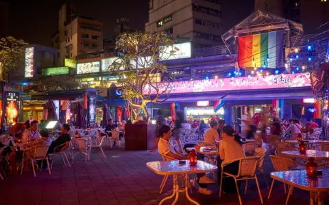 A vibrant night scene in gay Taipei, with people dining outdoors under colorful lights and a rainbow flag.