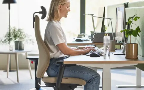 En kvinna sitter ergonomiskt vid ett skrivbord och arbetar vid datorn.