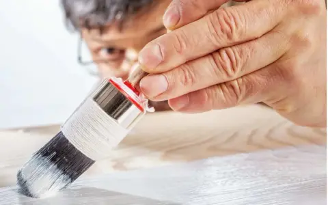 Un uomo applica il primer per legno con un pennello, preparando la superficie per la verniciatura.