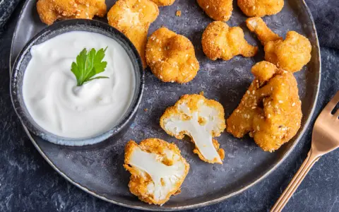 Knusprige Blumenkohl Nuggets aus dem Ofen, goldbraun paniert und mit Sesam bestreut, serviert mit einem cremigen Dip.