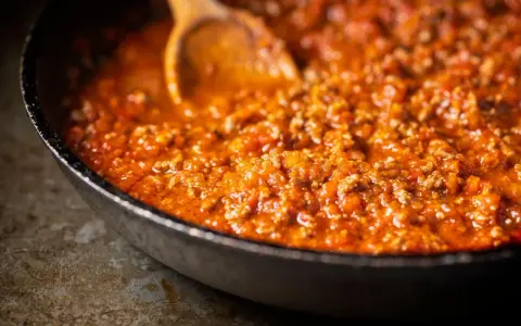 Herzhafte Bolognese-Sauce köchelt in einer Pfanne, die Zutaten für ein perfektes Pastagericht. Ein Holzlöffel rührt die köstliche Masse.