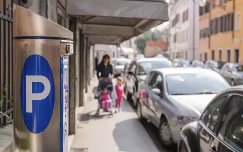 Parkomat z symbolem "P" i w tle kobieta z dziećmi na wózku, a obok samochody. Czy to parkowanie w miejscu niedozwolonym?