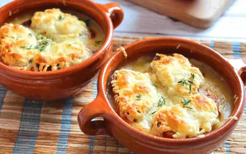 Dos cazuelas de barro con sopa de cebolla gratinada con queso y hierbas.