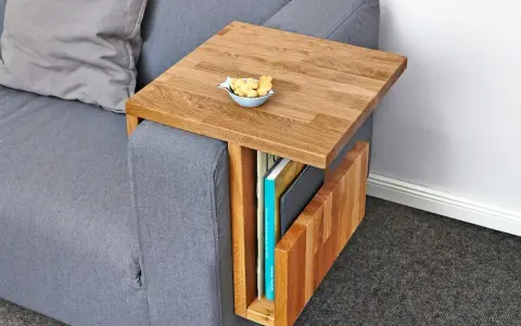Ett smart diy soffbord i trä som hängs över armstödet på en grå soffa. Perfekt för att förvara böcker och ha en skål med kex nära till hands.