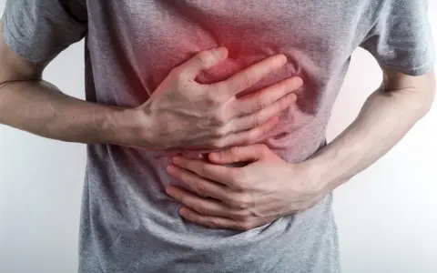 Osoba trzyma się za brzuch, odczuwając ostry ból w klatce piersiowej na środku. Czerwony obszar na koszulce sugeruje miejsce dolegliwości.