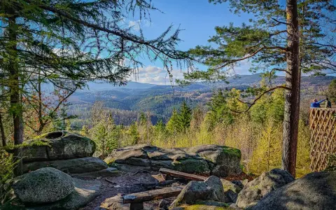 Kamienne skały i ławki na tle rozległej, leśnej panoramy Karkonoszy.