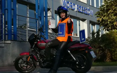 Uśmiechnięta motocyklistka z dokumentem w ręku i kciukiem w górze, gotowa na egzamin teoretyczny kat A.