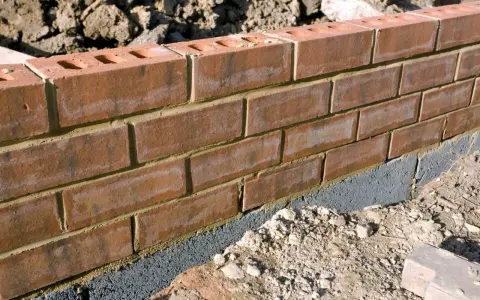 Ceglana ściana ogrodzenia z widoczną warstwą izolacyjną, która stanowi alternatywę dla tradycyjnej podmurówki.