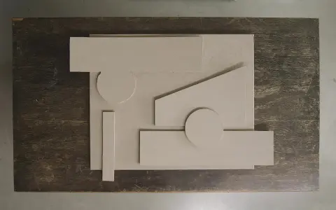 Abstrakt komposition med geometriska former i ljusbeige akrylfärg, arrangerade på en mörk träyta.