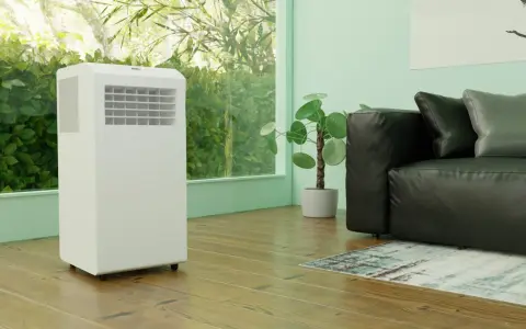 Biały klimatyzator przenośny stoi obok czarnej kanapy. Czy warto zainwestować w taki sprzęt?