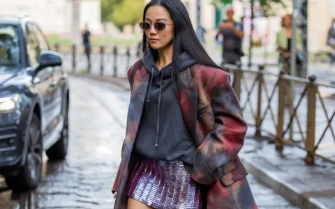 Frau in stylischem Outfit mit pailletten hose, Hoodie und gemustertem Blazer.