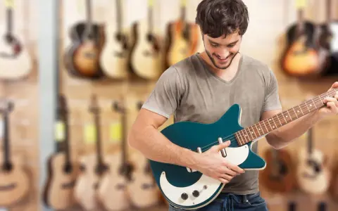 Uśmiechnięty mężczyzna testuje gitarę elektryczną w sklepie muzycznym. W tle widać wiele innych instrumentów.