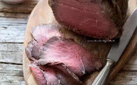 Roast beef ricetta classica: succulento arrosto affettato su tagliere di legno, pronto per essere gustato.