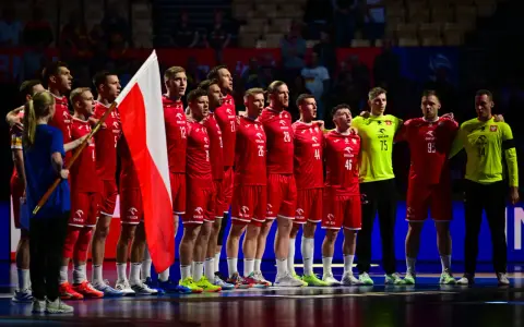 Drużyna piłkarzy ręcznych w czerwonych strojach z polską flagą. To ważny moment w 2 lidze piłki ręcznej.