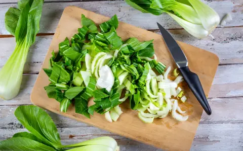 Frischer Pak Choi wird auf einem Holzbrett zerteilt, bereit zum Zubereiten. Ein Messer liegt daneben.