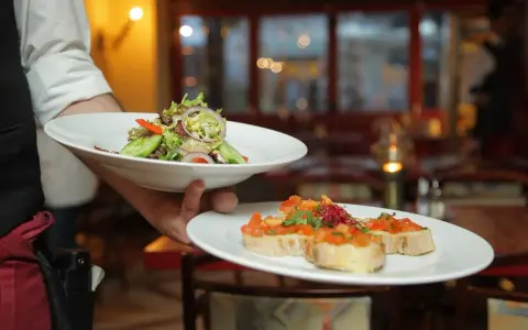 Un camarero experto demuestra cómo servir una mesa, presentando un plato de ensalada fresca y bruschettas.