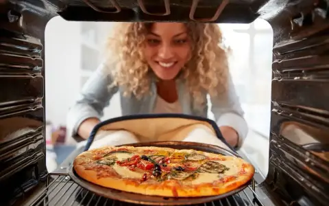 Uśmiechnięta kobieta wyjmuje z piekarnika pyszną, gorącą pizzę. Właśnie skończyła piec pizzę i jest gotowa do jedzenia.
