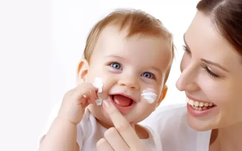 Uśmiechnięty maluch z białymi plamkami kremu na policzkach. Sudocrem na co? Na delikatną skórę dziecka, chroniąc ją i łagodząc.