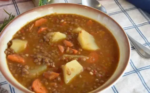 Un plato humeante de lentejas estofadas al estilo Arguiñano, con patatas y zanahorias, listo para disfrutar.