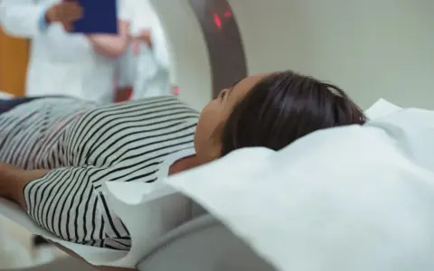 Kobieta leży na stole do rezonansu magnetycznego. Czy na rezonans magnetyczny można mieć hybrydy? Lekarz w białym fartuchu obserwuje badanie.