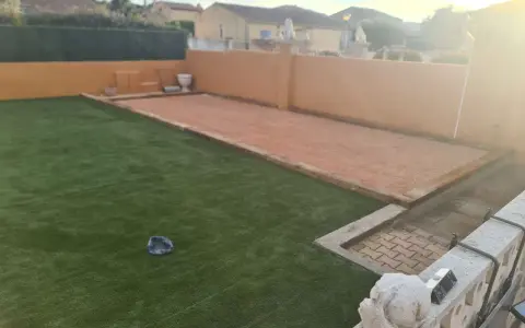 Un terrain de pétanque prêt pour l'entretien, avec une allée en gravier et une pelouse artificielle.