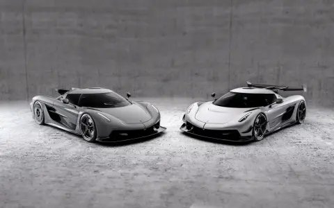 Dwa lśniące Koenigsegg Jesko, jeden szary, drugi srebrny, stoją obok siebie na betonowym tle, gotowe do wyścigu.