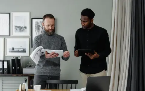 Two men review documents and a tablet, discussing the details of in-kind donation accounting.