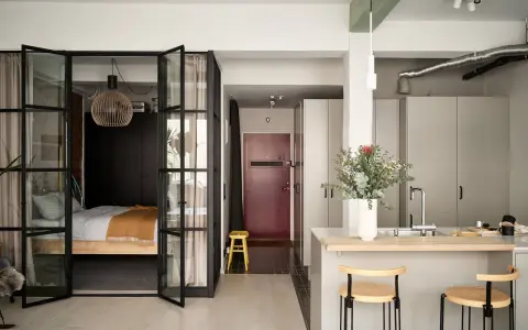 Une chambre en second jour, séparée par des portes vitrées. Une cuisine moderne avec un îlot et des tabourets complète l'espace.