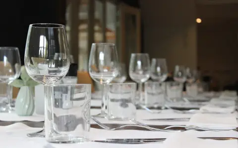 Un verre à eau et un verre à vin sont positionnés sur une table dressée, prêts pour un repas.