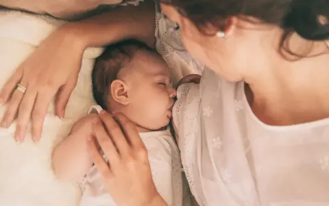Delikatne karmienie noworodka. Mama czule tuli dziecko, które śpi, ssąc pierś. Wskazówki, jak wybudzić noworodka do karmienia, mogą być pomocne w takich chwilach.