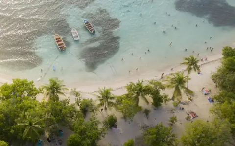 Rajska plaża na Gwadelupie Francuskiej. Ludzie kąpią się w turkusowej wodzie, łodzie kołyszą się przy brzegu, a palmy szumią nad piaszczystą plażą.