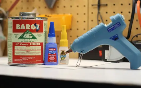 A hot glue gun, Barge cement, Loctite super glue, and Gorilla Super Glue are on a workbench. Does Gorilla Glue melt? This image shows various adhesives.
