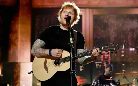 Ed Sheeran spielt Gitarre und singt auf einer Bühne.