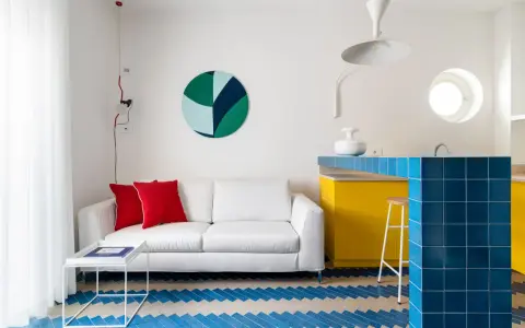 Sofá blanco, cojines rojos y suelo con **estilos de diseño** geométricos. Barra de cocina azul brillante y gabinetes amarillos vibrantes.