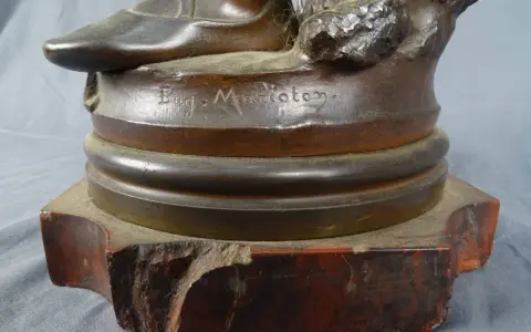 Signature "Eug. Marioton" gravée sur la base d'une sculpture en bronze patiné, posée sur un socle en marbre rouge.