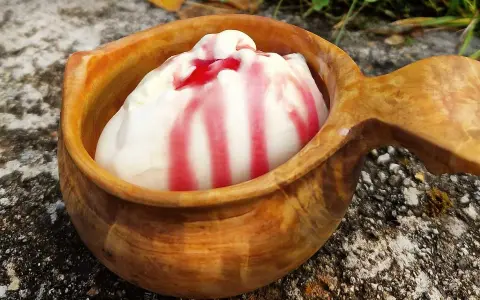 En skopa hemmagjord glass med röd sås i en träkopp, placerad utomhus på sten.