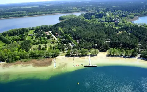 Malownicze warchały jezioro otoczone lasem, z piaszczystą plażą, pomostami i kolorowymi łódkami.