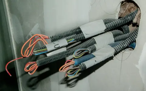Przewody elektryczne w peszlach wychodzące ze ściany, gotowe do połączenia. Widać kolorowe żyły: pomarańczowe, niebieskie, brązowe, zielono-żółte.