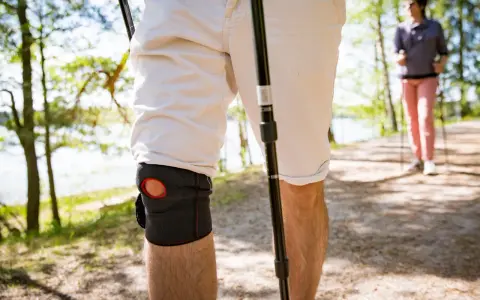 Mann mit Kniebandage beim Nordic Walking. Knieschmerzen beim Bergabgehen beeinträchtigen die Wanderung.