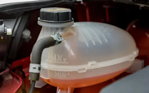 A car's coolant reservoir with MAX and MIN lines. The orange coolant is between the lines, indicating the correct level. This image helps answer "what coolant does my car need.